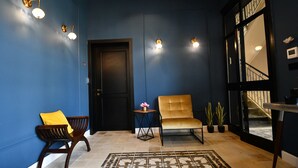 Un pasillo con paredes azules, un banco de madera, una pequeña mesa con una flor y una silla.