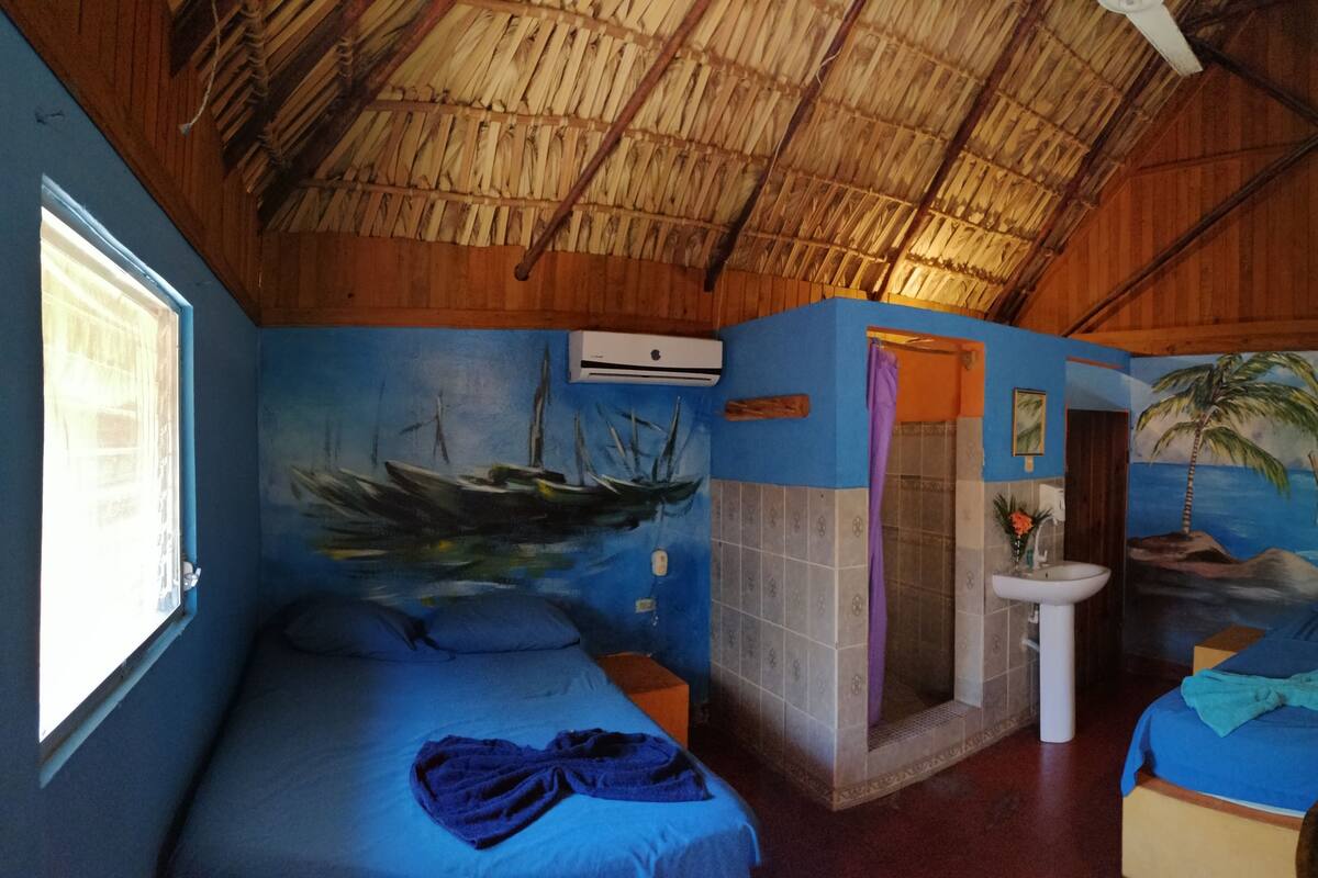 A room with two beds, a sink, and a mural of a boat and palm trees.