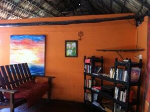 A room with a thatched roof, a red couch, a bookshelf, and a painting of a sunset.