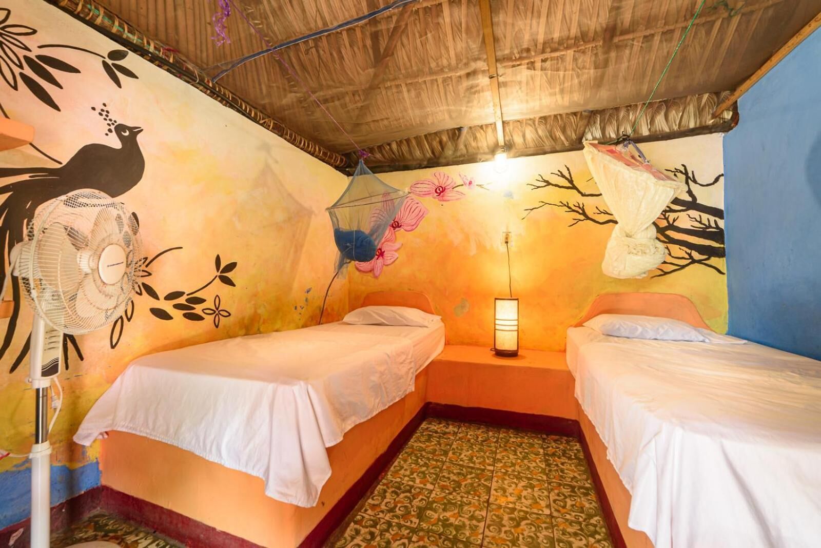 A room with two beds, a fan, a wall mural, and a hanging net.