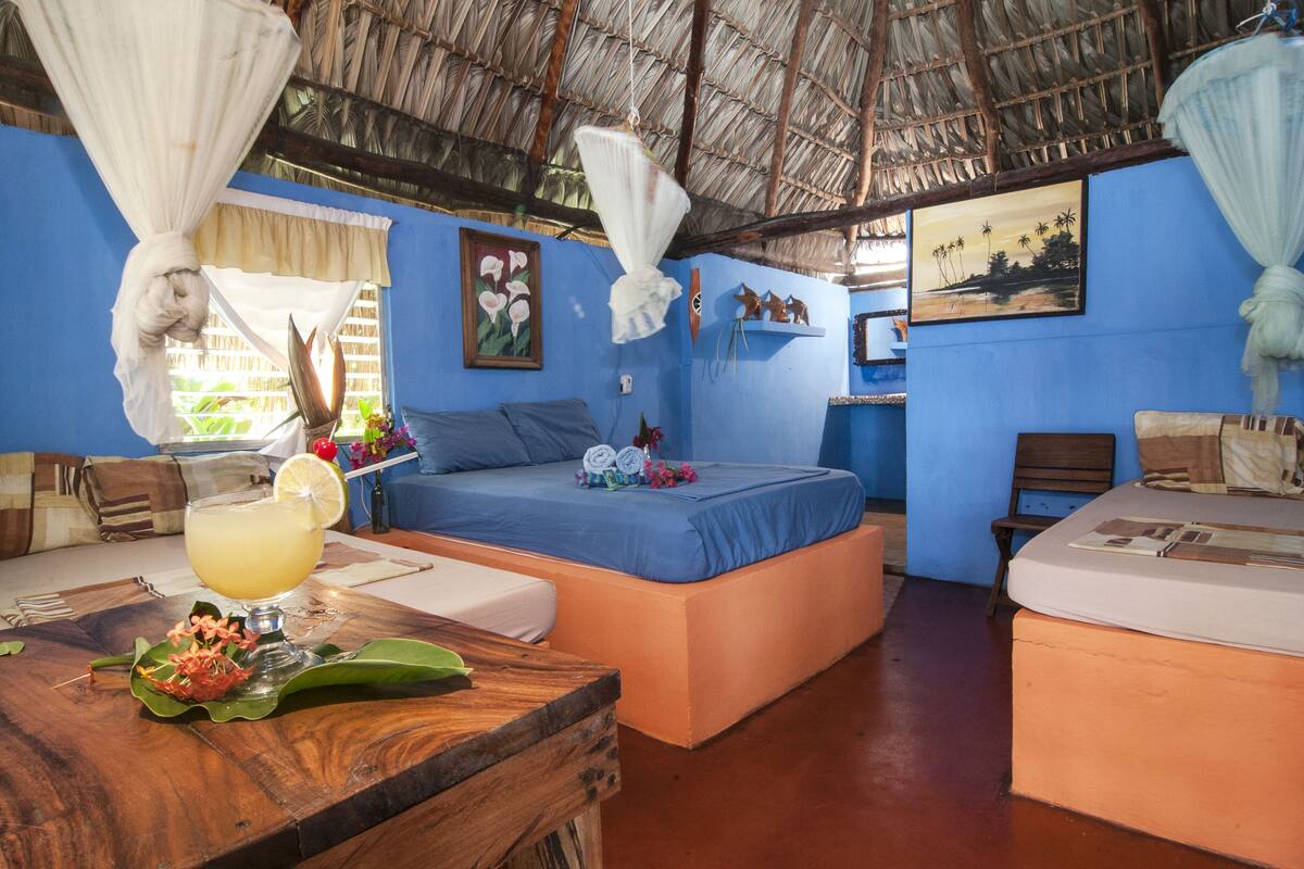 A room with a bed, a table with a drink, and a chair.