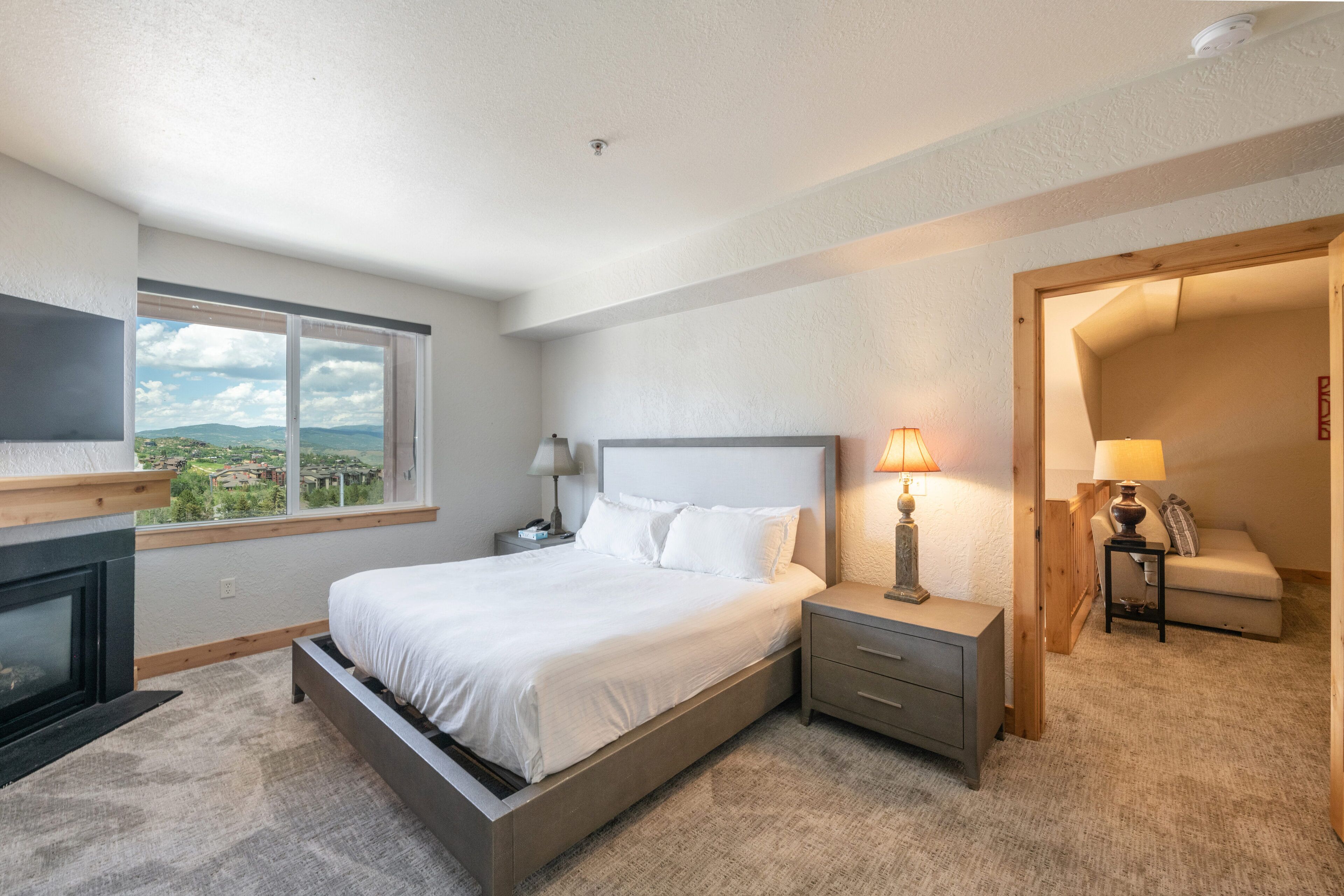 A bedroom with a bed, bedside tables, a lamp, a TV, and a view of the outdoors.