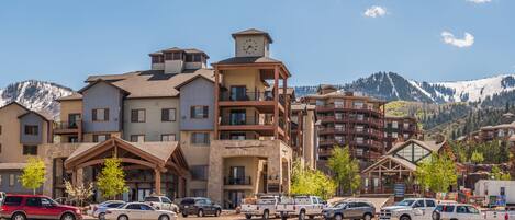 A multi-story hotel with a clock tower, balconies, and a view of snow-capped mountains.