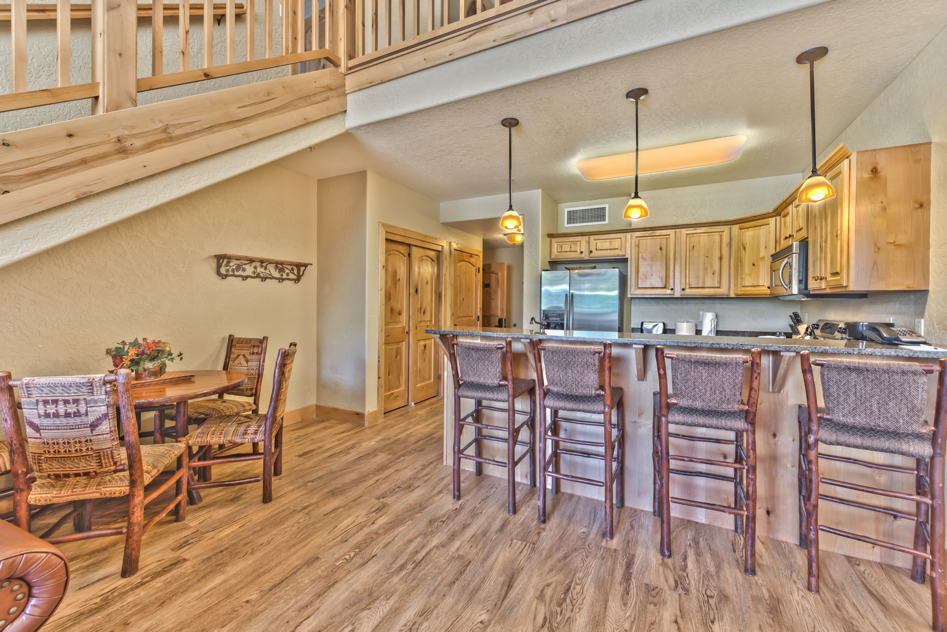 A spacious kitchen with wooden cabinets, a central island with bar stools, a dining area with a table and chairs, and a staircase leading to an upper level.