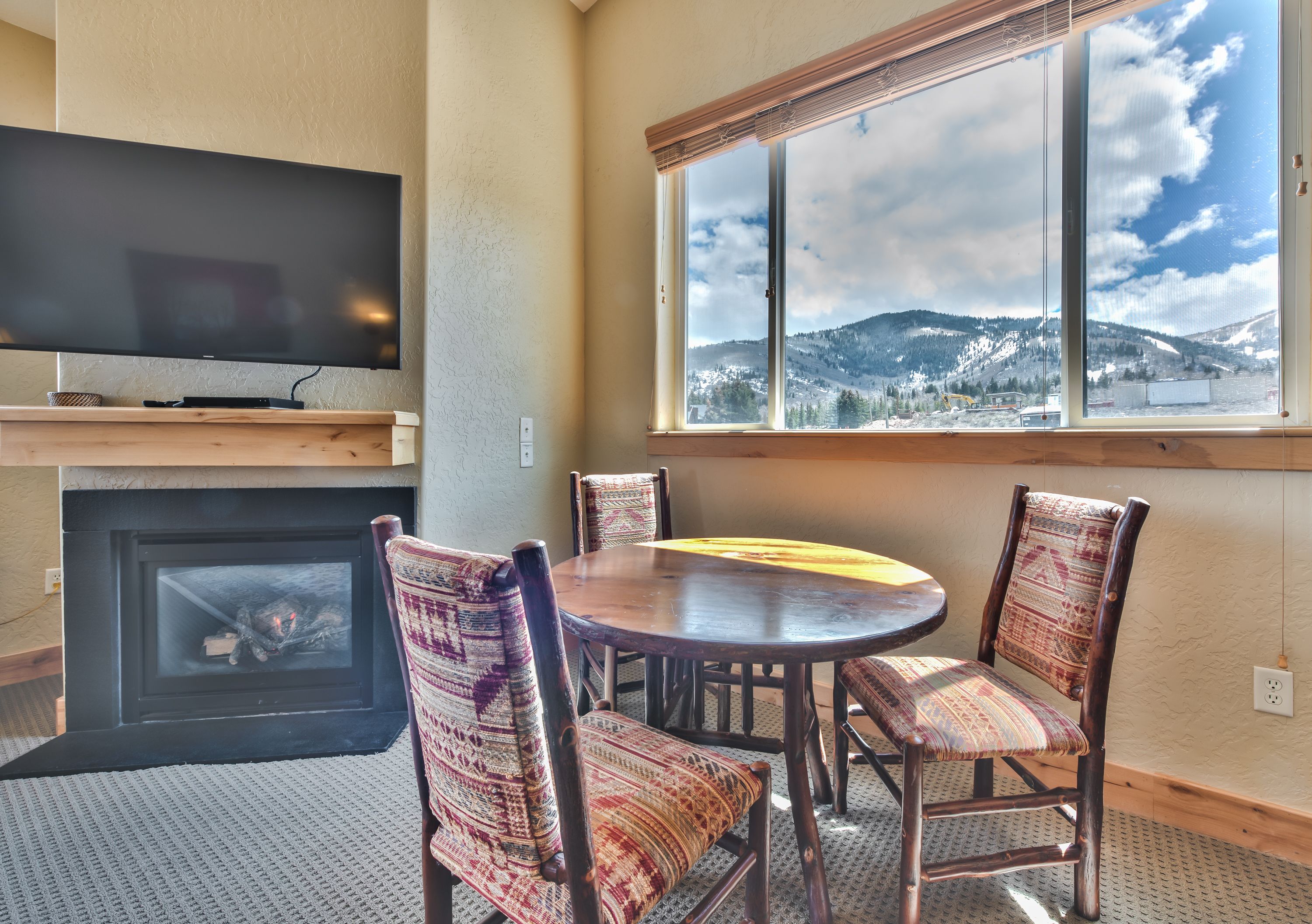 A cozy room with a fireplace, a television mounted above it, and a large window offering a mountain view.