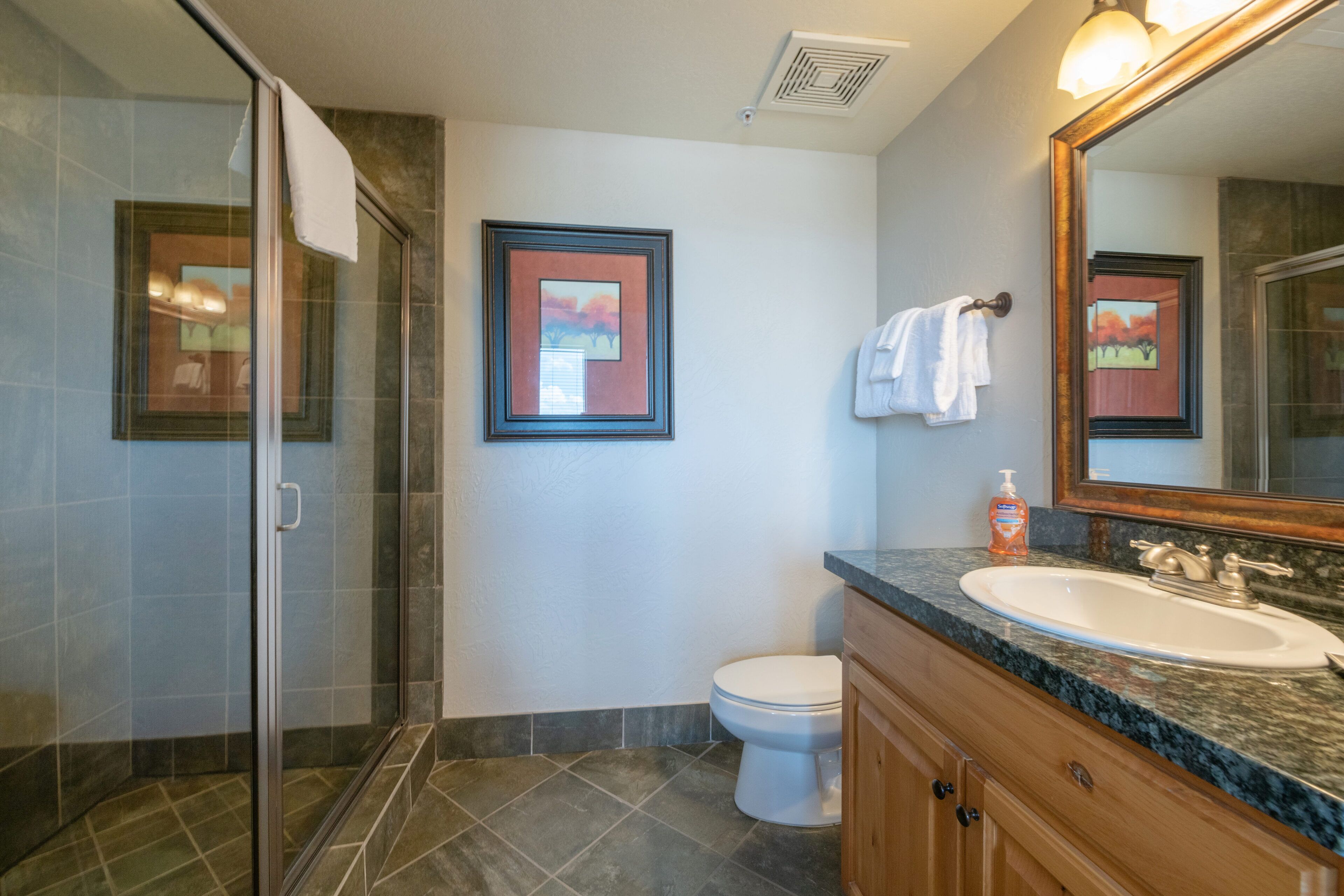 A bathroom with a glass shower enclosure, a white toilet, a sink with a marble countertop, and wooden cabinets.