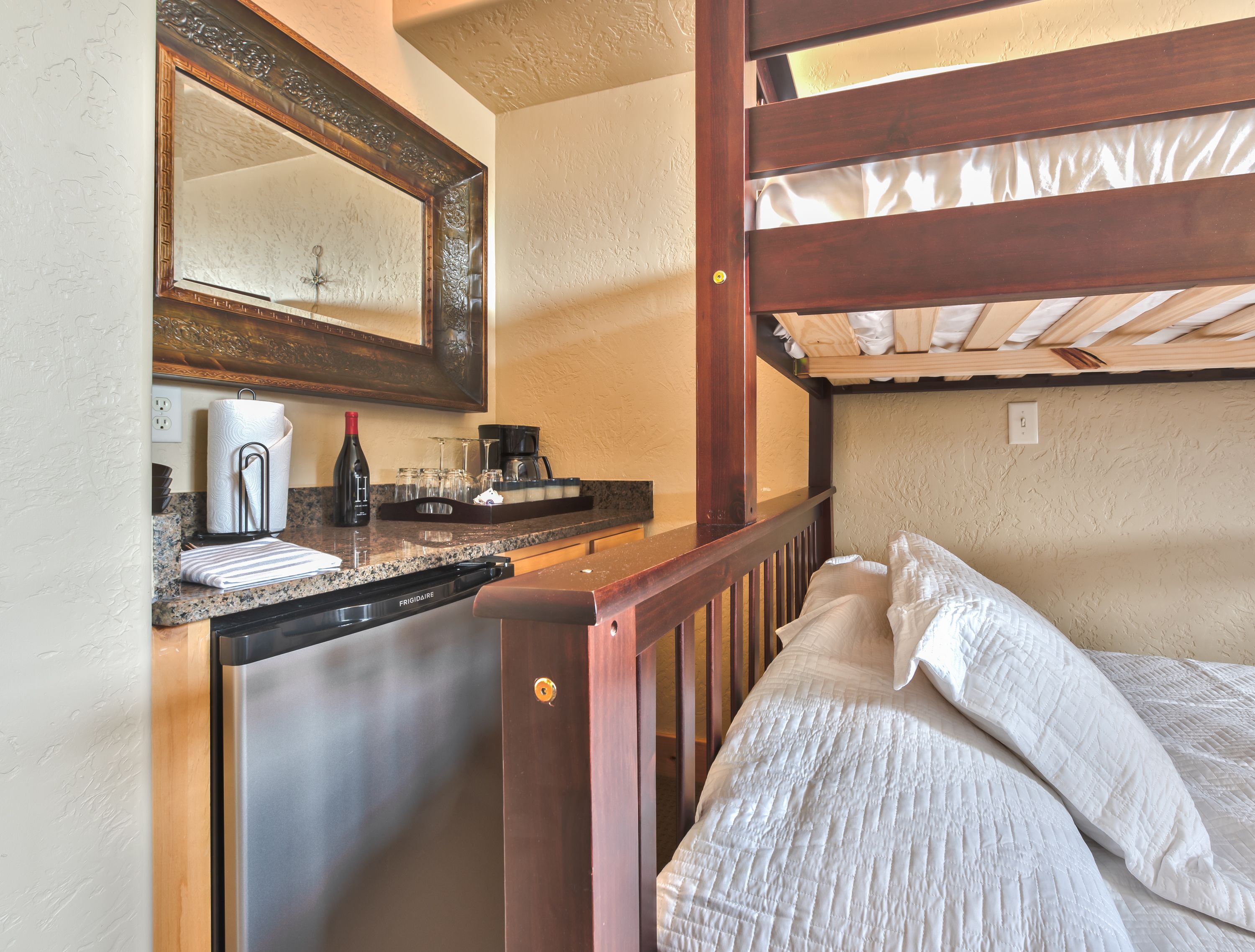 Una cocina compacta con refrigerador, lavamanos y encimera. Hay una cama de madera con ropa de cama blanca y cabecera de madera.