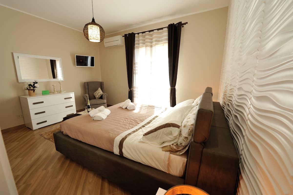 A bedroom with a bed, a dresser, a chair, a television, and a window with curtains.