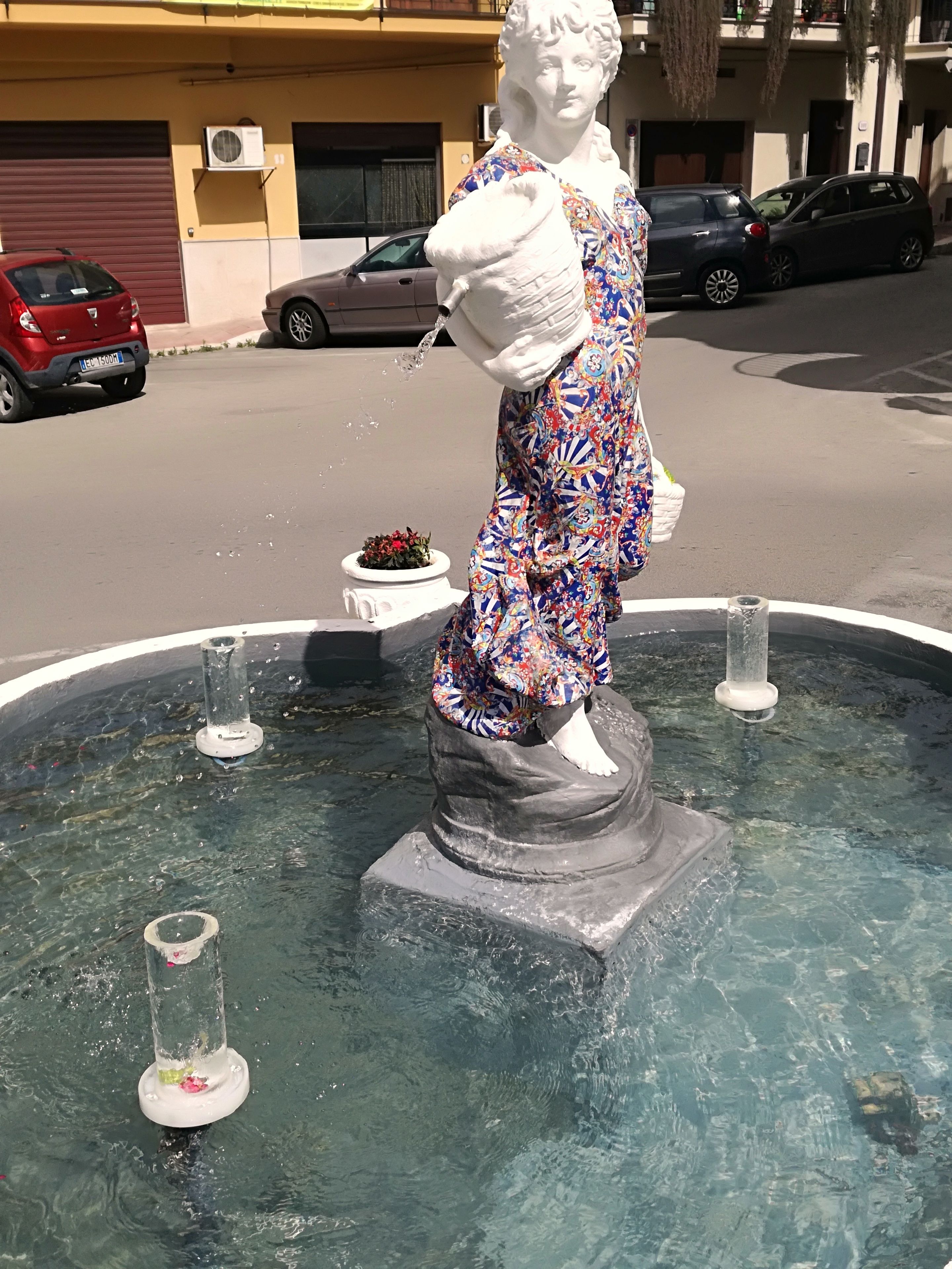 Une statue dans une fontaine, vêtue d’une robe colorée, et entourée d’un bassin d’eau claire.