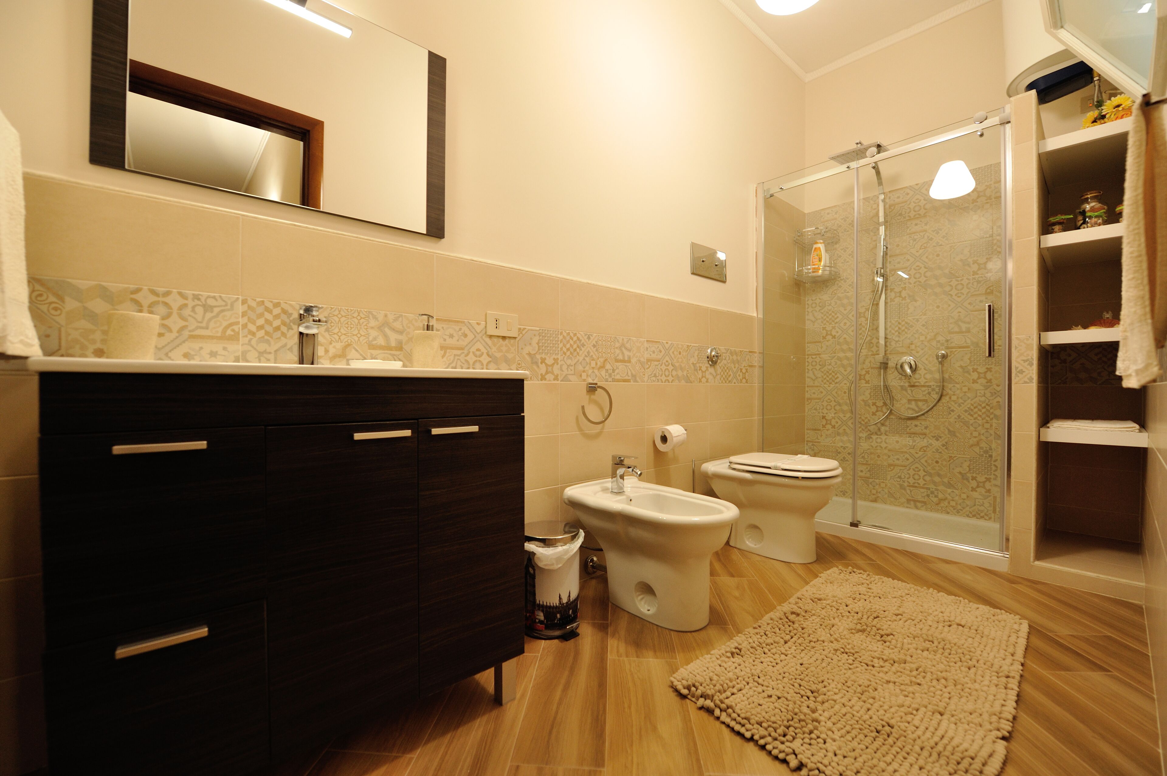 Un baño moderno con tocador de madera oscura, un bidé, un inodoro y una zona de ducha con mampara de vidrio.
