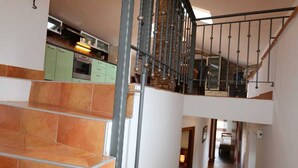 Un interior de varios niveles con una escalera, una zona de cocina y un pasillo que conduce a otra habitación.