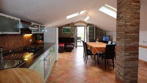 Una cocina con zona de comedor, un pilar de piedra y un televisor.