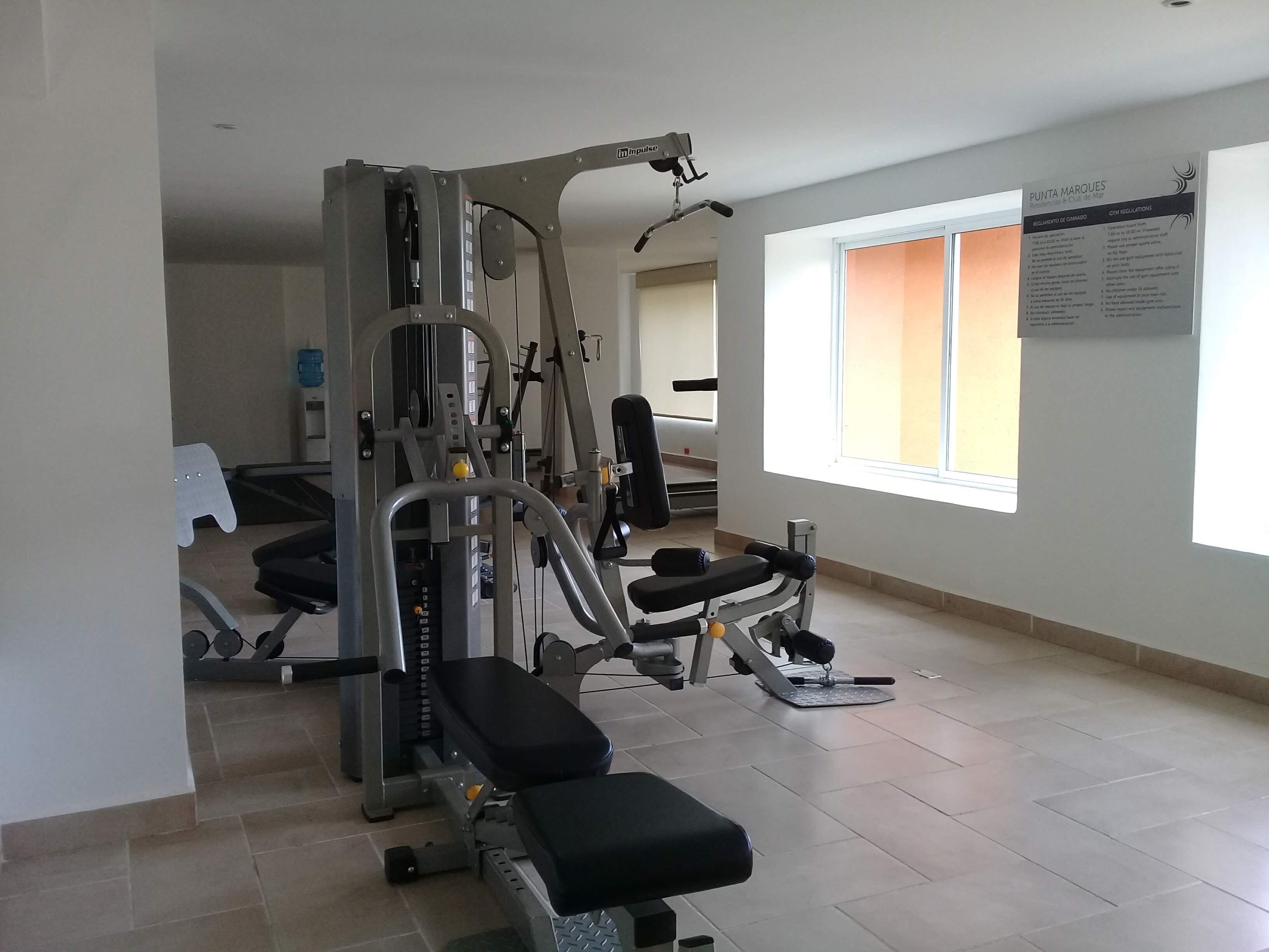 Una sala de gimnàstica amb equip d'exercici, una banca i una finestra amb vista.