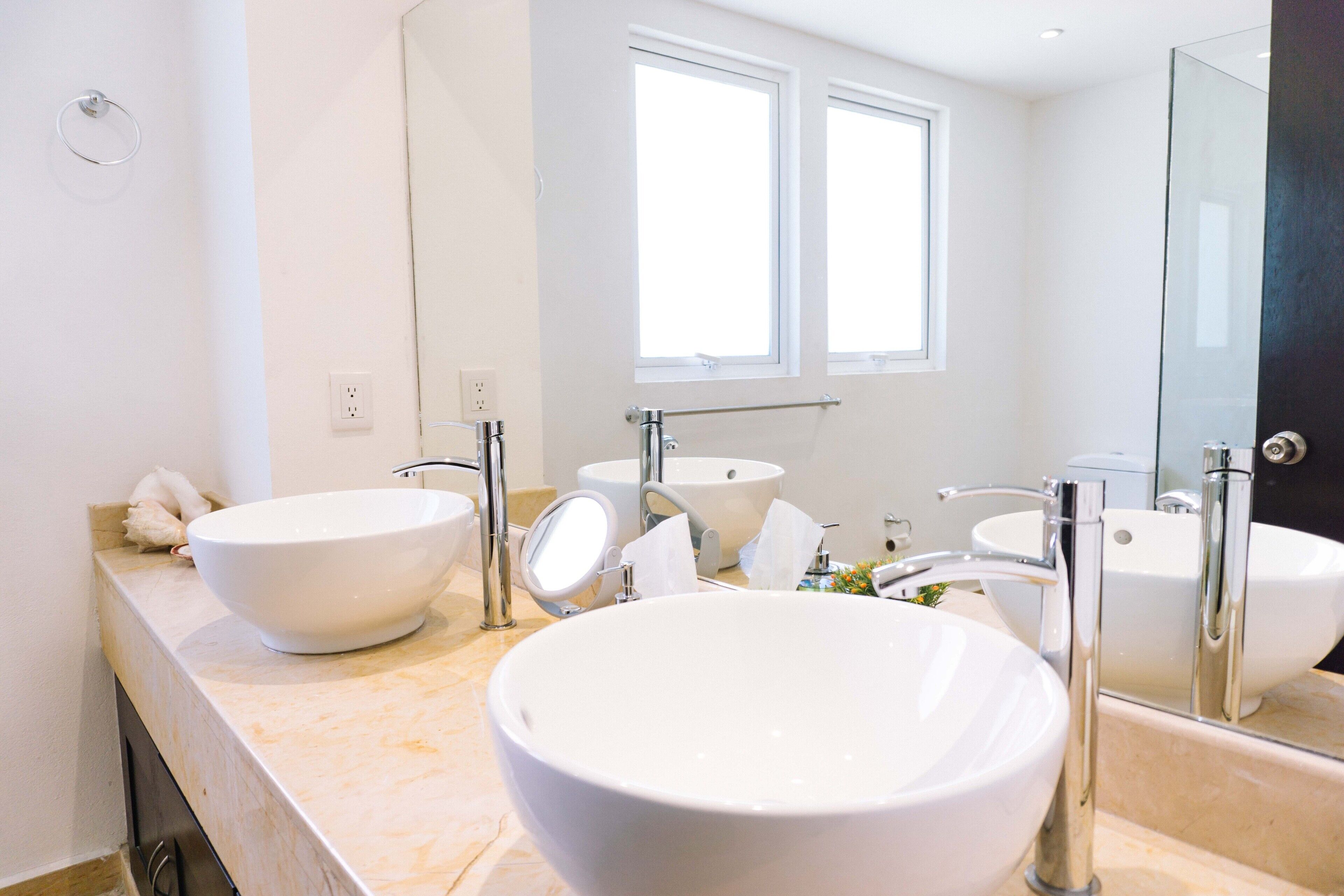 A modern bathroom with two large white sinks, a glass shower enclosure, and a large mirror.