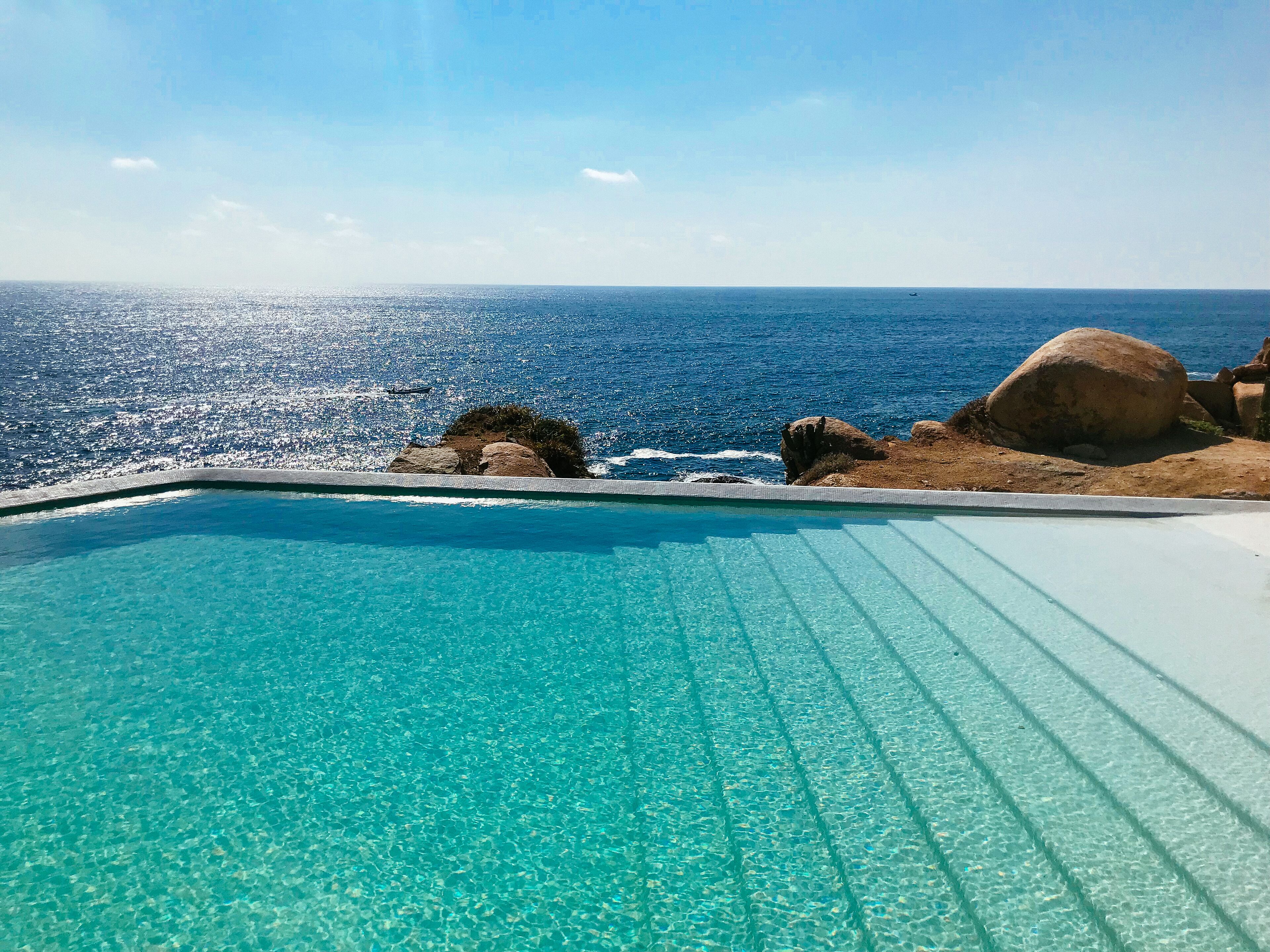 Una piscina azul cristalina con vistas al océano y terreno rocoso.