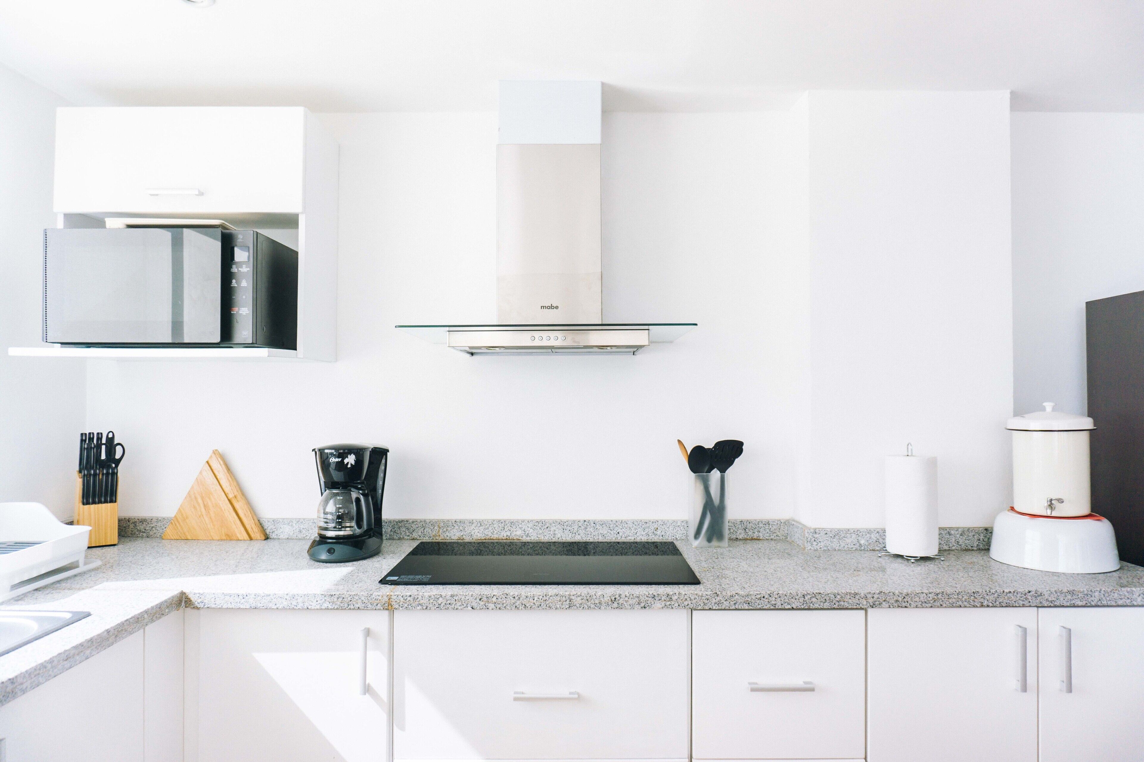 A modern kitchen with white cabinetry, a built-in microwave, a coffee maker, and a blender on the countertop.