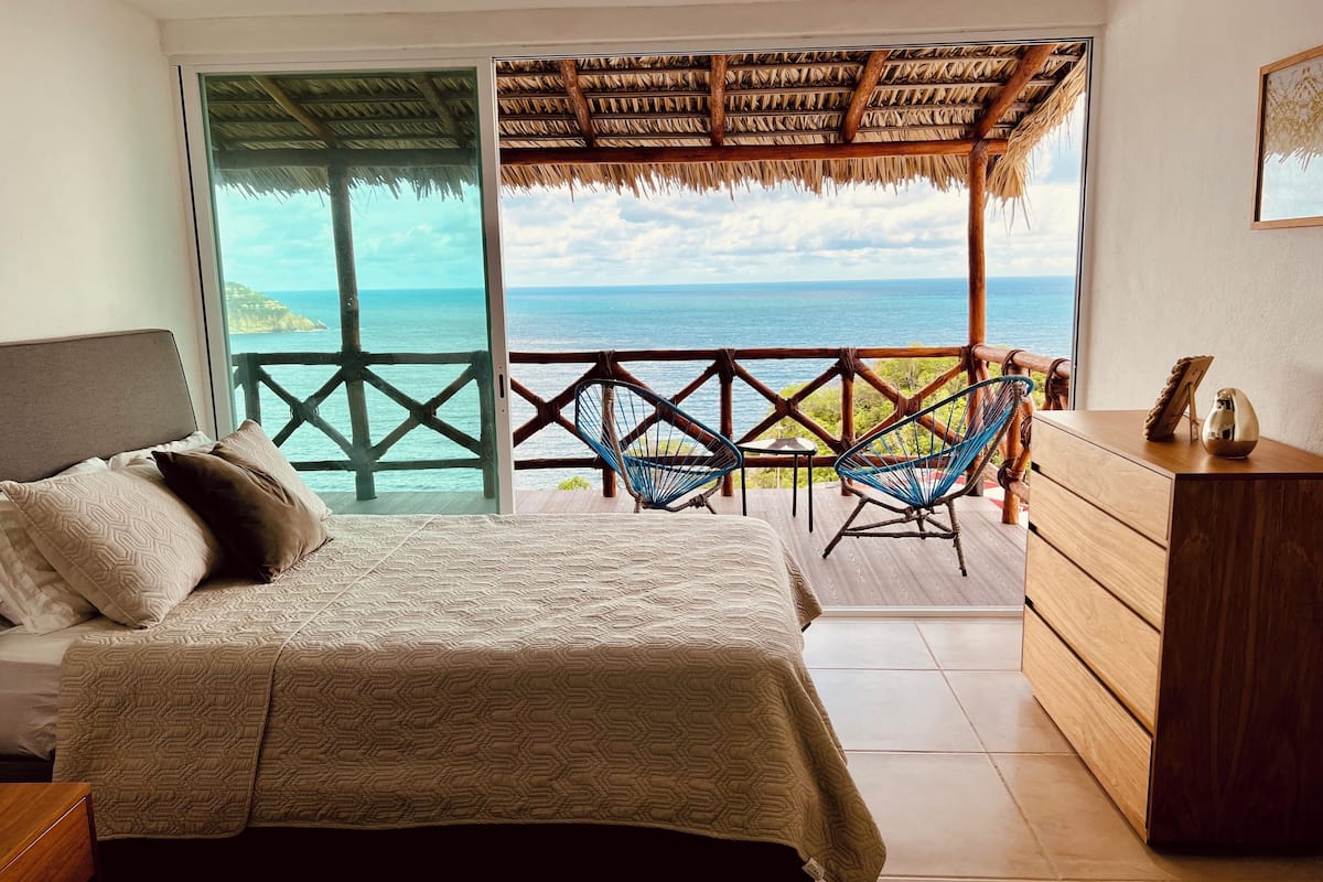 Un dormitorio con cama, cómoda de madera y balcón con vista al océano.