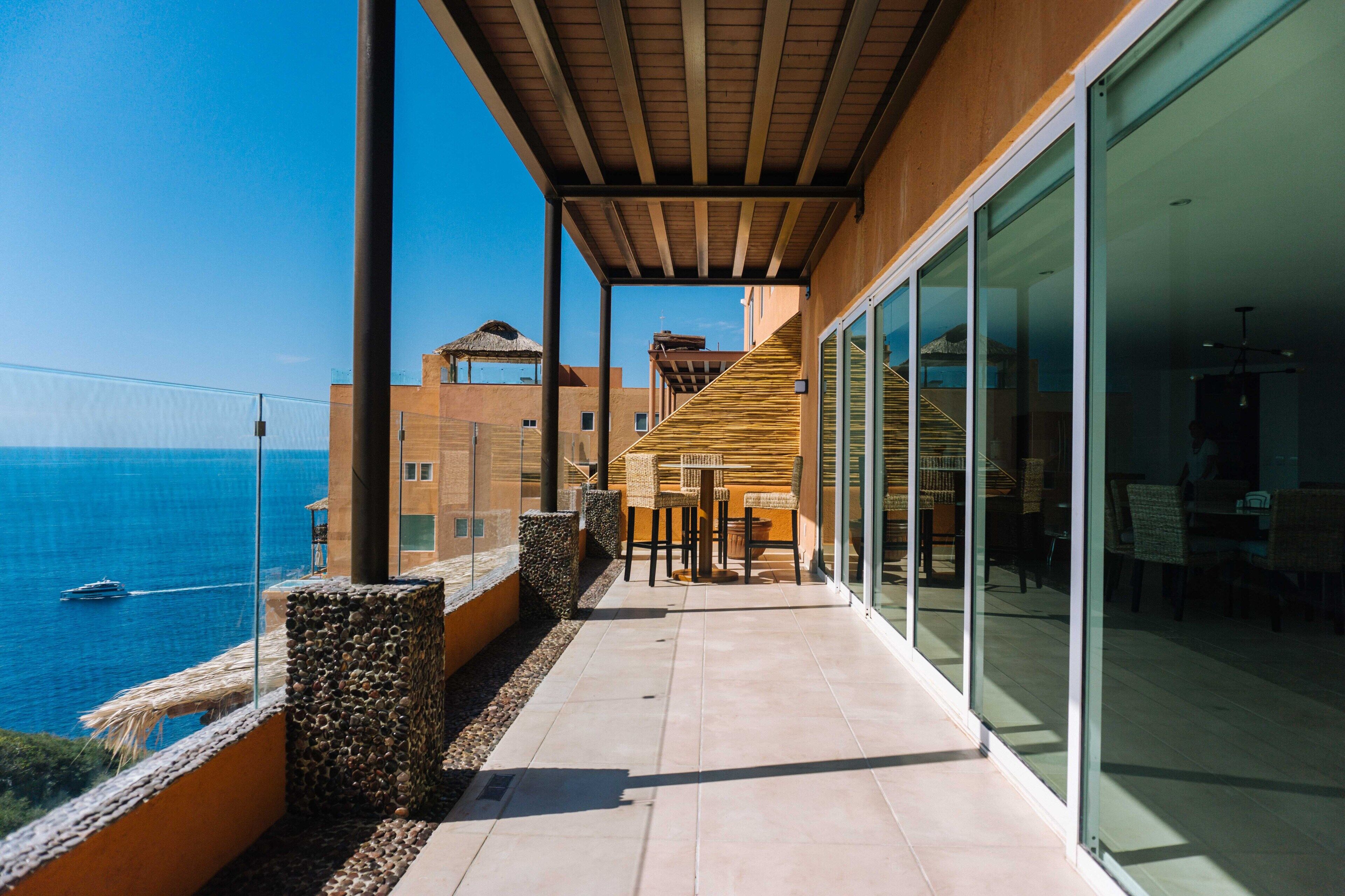 Een balkon met uitzicht op zee, een houten pergola en een glazen deur die naar een binnenruimte leidt.