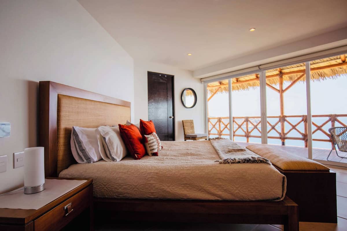 Habitación de hotel con una cama grande, una mesita de noche, una silla y un balcón con vistas.