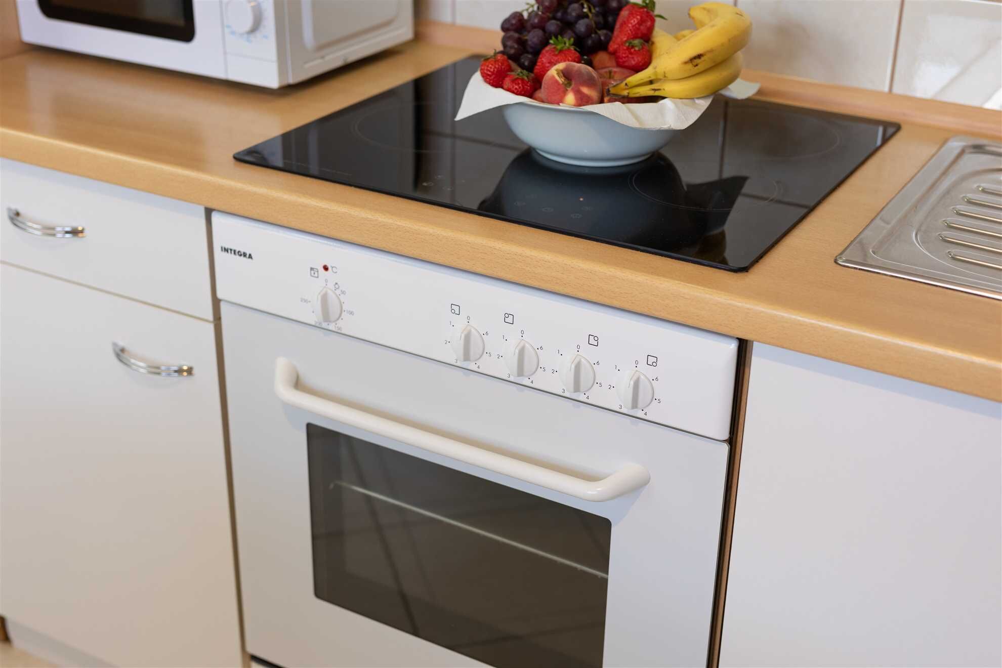 Une cuisine équipée d’un four encastré, d’un four à micro-ondes et d’un saladier rempli de fruits posé sur le plan de travail.