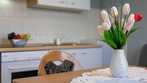 A kitchen with white cabinets, a bowl of fruit on the counter, and a vase with tulips on a table. - Apartment Padjen A2 (Silo - island Krk)