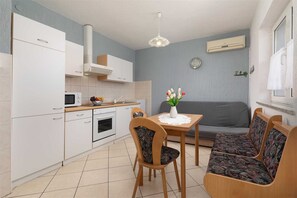 Une cuisine de taille réduite avec des meubles blancs, un four à micro-ondes et une cuisinière. On y trouve un coin repas avec une table et des chaises, ainsi qu’un canapé gris.