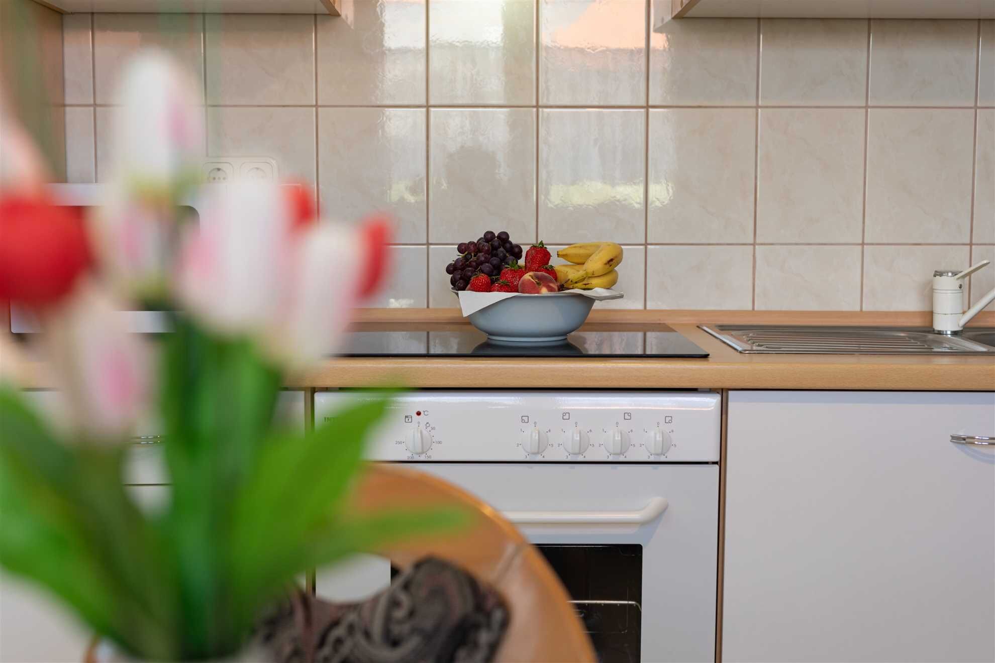 Una cocina con estufa blanca, un lavabo y un bol de fruta en la encimera.