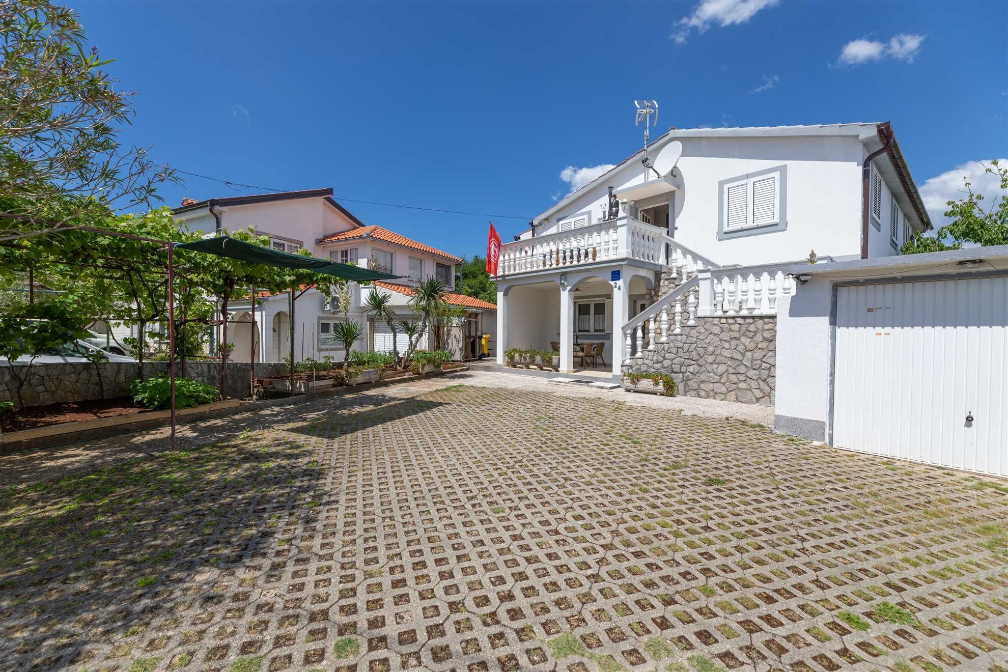 Un patio con pavimento de adoquines, un edificio blanco con balcón y un muro de piedra.