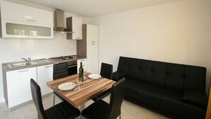 A compact kitchen with white cabinets, a black sofa, and a dining table with chairs. - Apartment Hodzic nr 3 (Silo - island Krk)