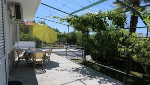 An outdoor patio with a table and chairs, a yellow umbrella, and a view of greenery and a fence. - Apartment Hodzic nr 3 (Silo - island Krk)