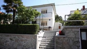A two-story building with a stone wall, a staircase, and a palm tree. - Apartment Hodzic nr 3 (Silo - island Krk)