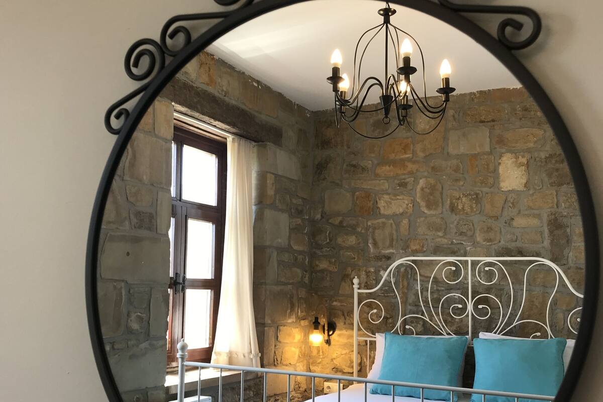 Quarto com parede de pedra, estrutura de cama de metal, lustre e espelho.
