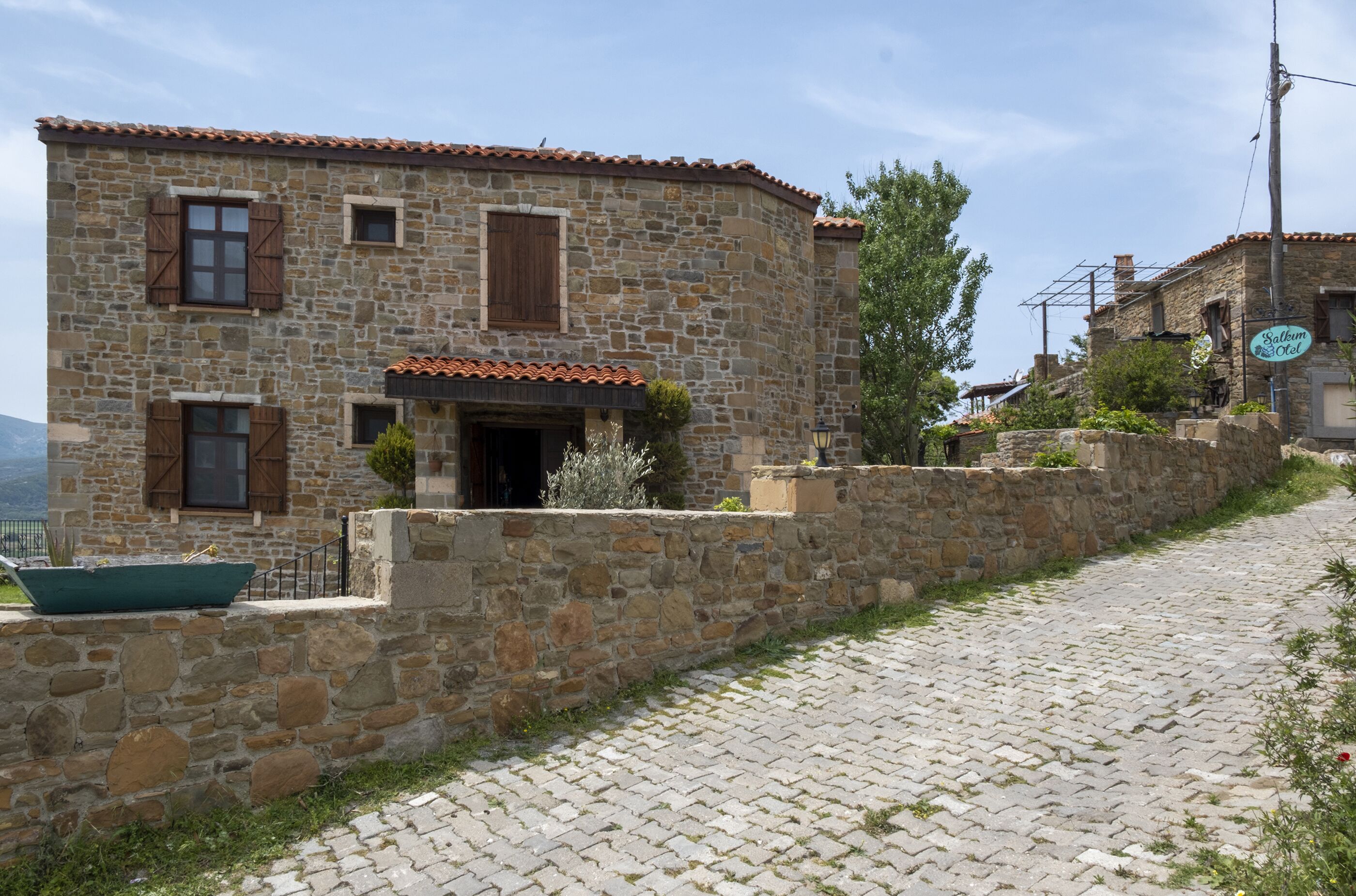 A stone building with a tiled roof, a stone wall, and a cobblestone path.