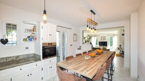 A spacious kitchen with white cabinetry, a wooden dining table, and modern lighting fixtures. - Pet friendly home in Baixas (Baixas)