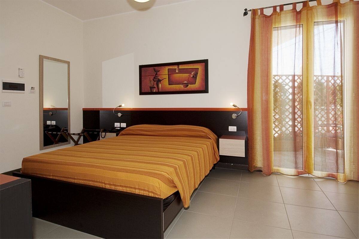 A bedroom with a bed, a nightstand, a wall-mounted TV, a painting, and a window with curtains.