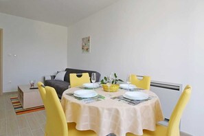 Uma sala de jantar com uma mesa posta para quatro pessoas, cadeiras amarelas, um sofá cinza e um pequeno quadro na parede.