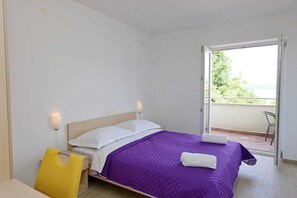 Quarto com cama, cadeira, mesa de cabeceira e vista para o exterior.