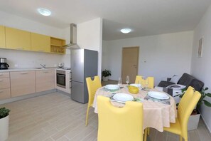 Uma cozinha compacta com eletrodomésticos modernos, uma área de refeições com cadeiras amarelas e um pequeno espaço de estar com sofá.