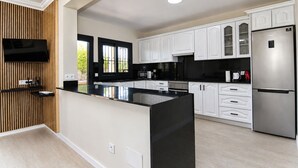 A modern kitchen with white cabinets, a black countertop, a stainless steel refrigerator, and a flat-screen TV mounted on a wooden panel. - Ca Na Coloma 145 fantastic villa with barbecue, billiards, ping pong and WiFi (Playa de Muro)