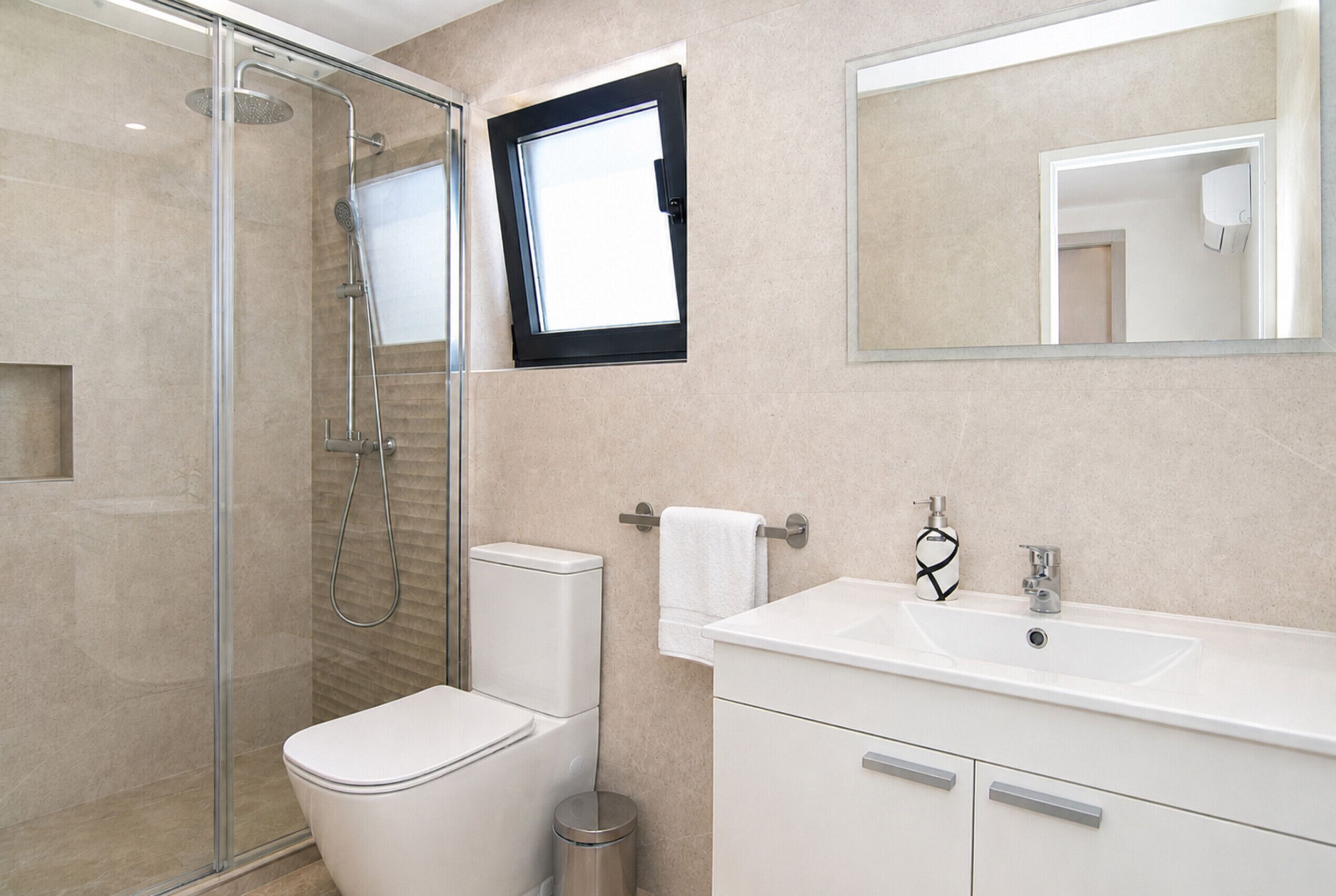Un baño moderno con ducha envuelta en vidrio, inodoro, lavamanos y espejo.