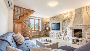 Een woonkamer met een stenen muur, een open haard, een televisie, een bank en een trap.