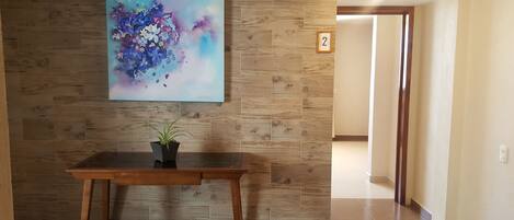 A wooden wall with a framed abstract painting, a small potted plant on a wooden table, and a door with a number '2' sign.