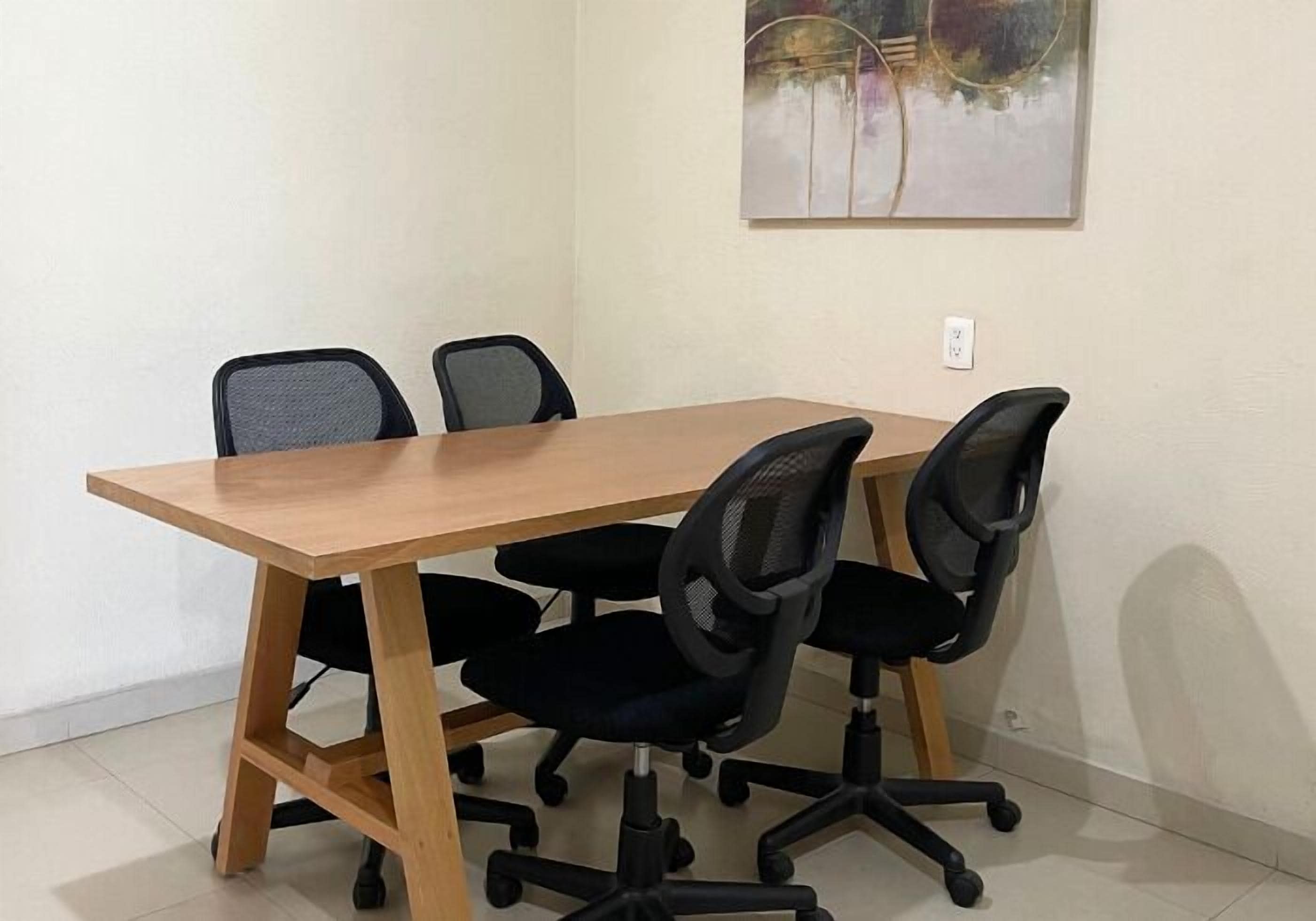 A conference room with a wooden table and four black office chairs.
