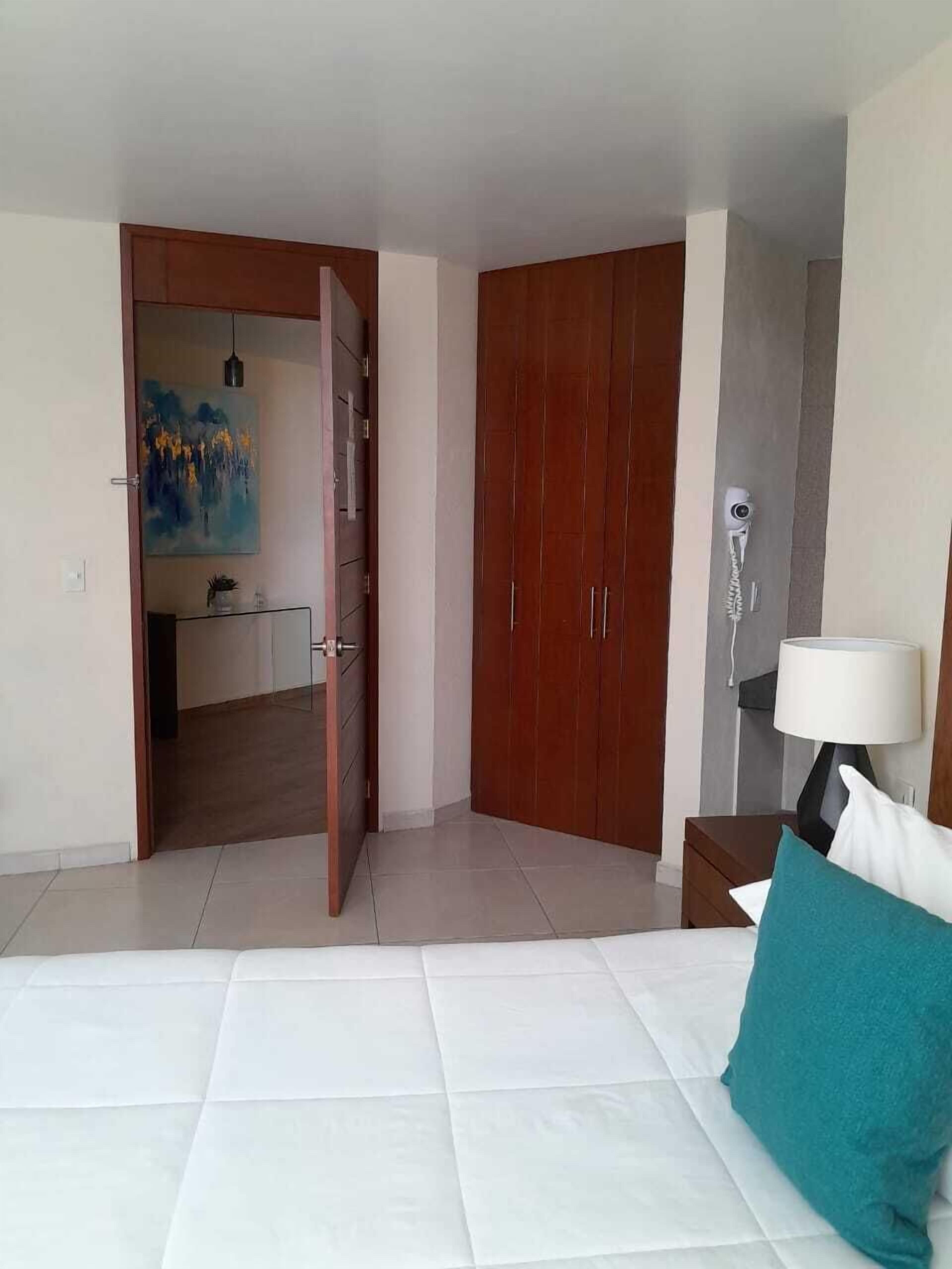 Habitación de hotel con cama, armario de madera, un cuadro en la pared y mesita de noche con lámpara.