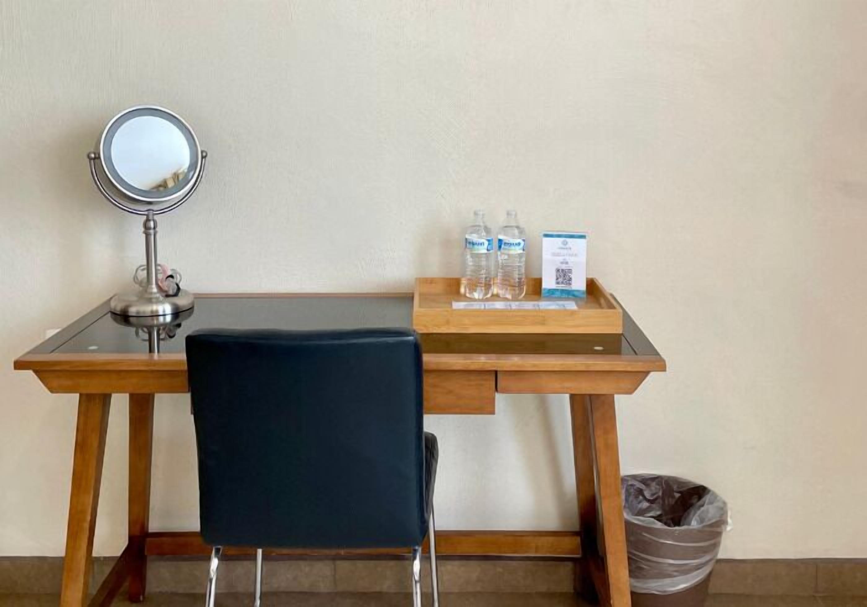 A hotel desk with a mirror, two water bottles, a tray with a box, and a trash bin.