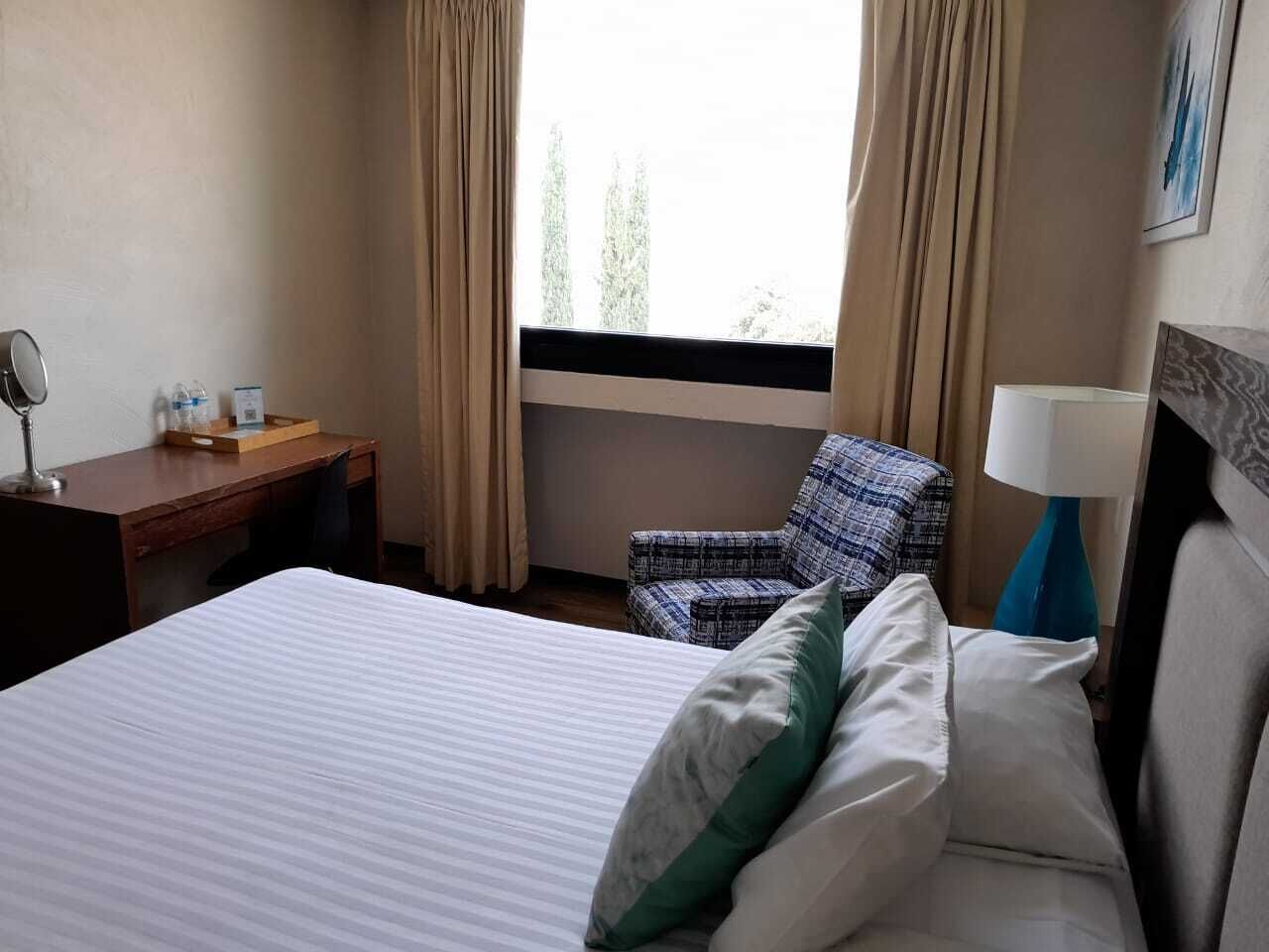 Ein Hotelzimmer mit einem Bett, einem Schreibtisch, einem Stuhl und einem Fenster mit Vorhängen.