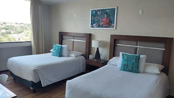 Habitación de hotel con dos camas, una mesita de noche con lámpara, un cuadro en la pared y una ventana con cortinas.