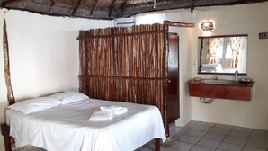 Una camera da letto con un letto di legno, un materasso bianco, una testiera in legno, un armadio in legno, un bagno con lavandino e specchio, e un pavimento piastrellato.