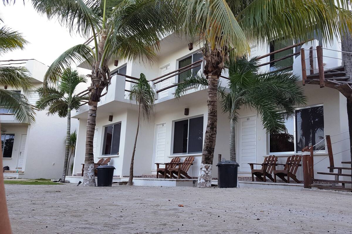 A two-story building with a balcony, palm trees, and outdoor seating.