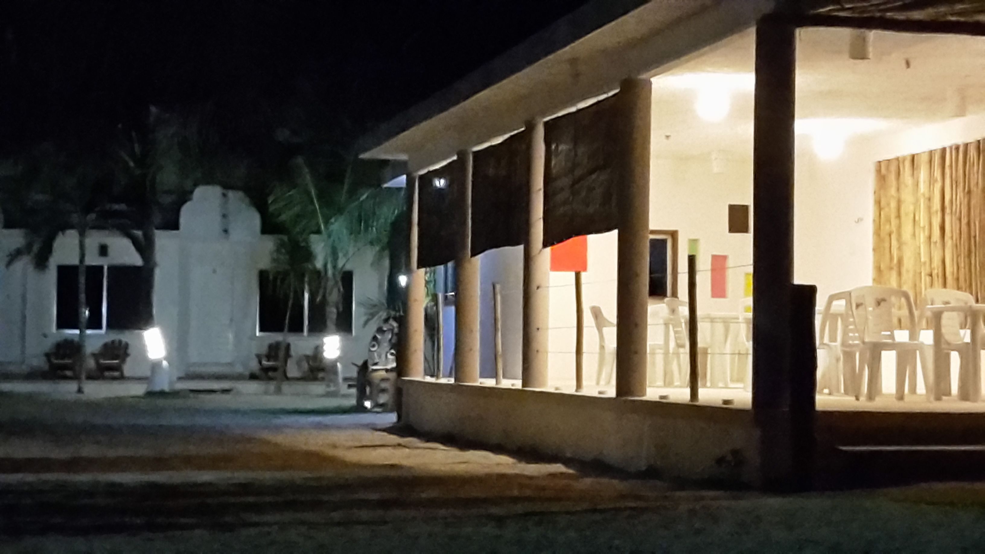 Un edificio con un espacio de asientos techado al aire libre, algunas sillas y una puerta de madera.